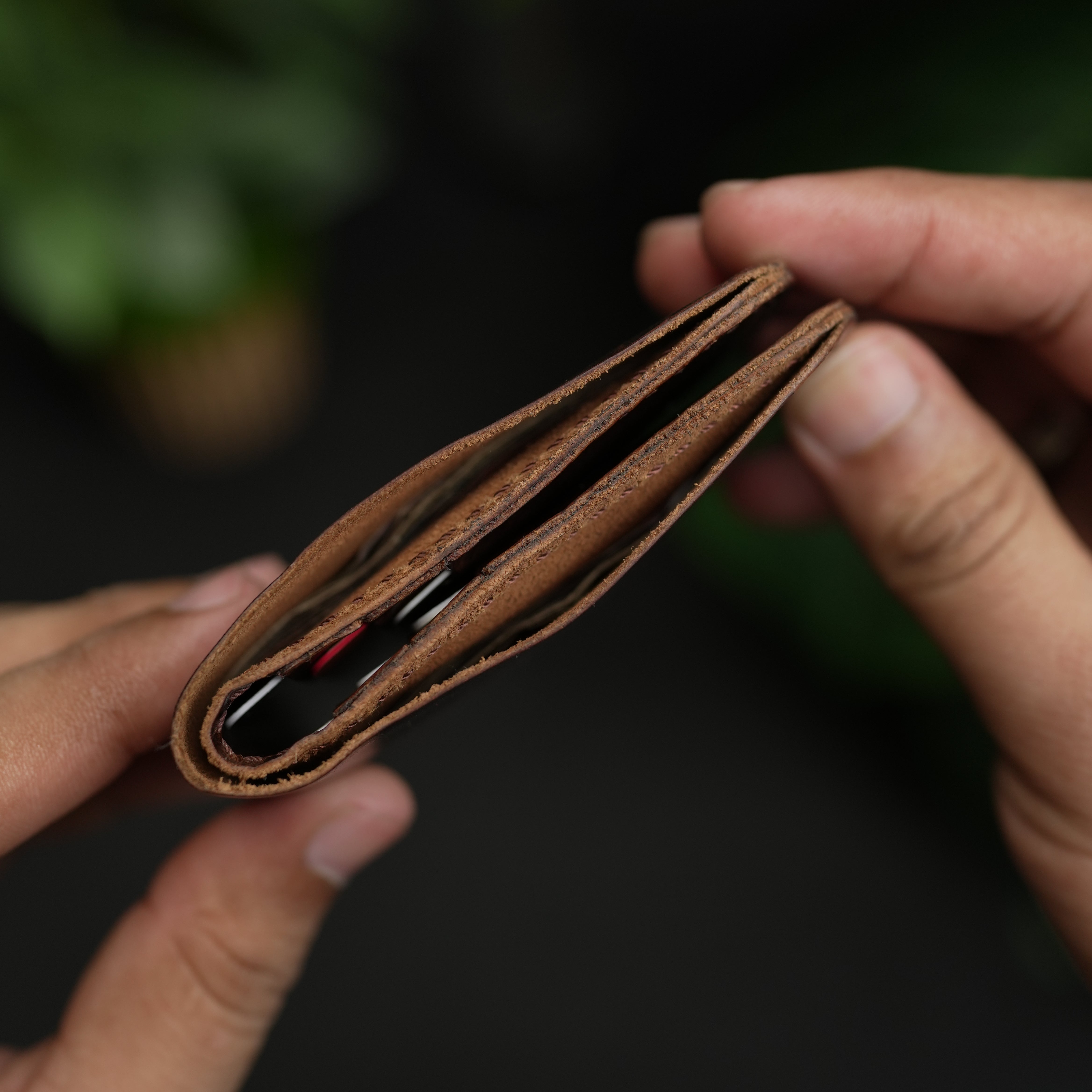 Brown leather wallet held by a person with a blurred green background
