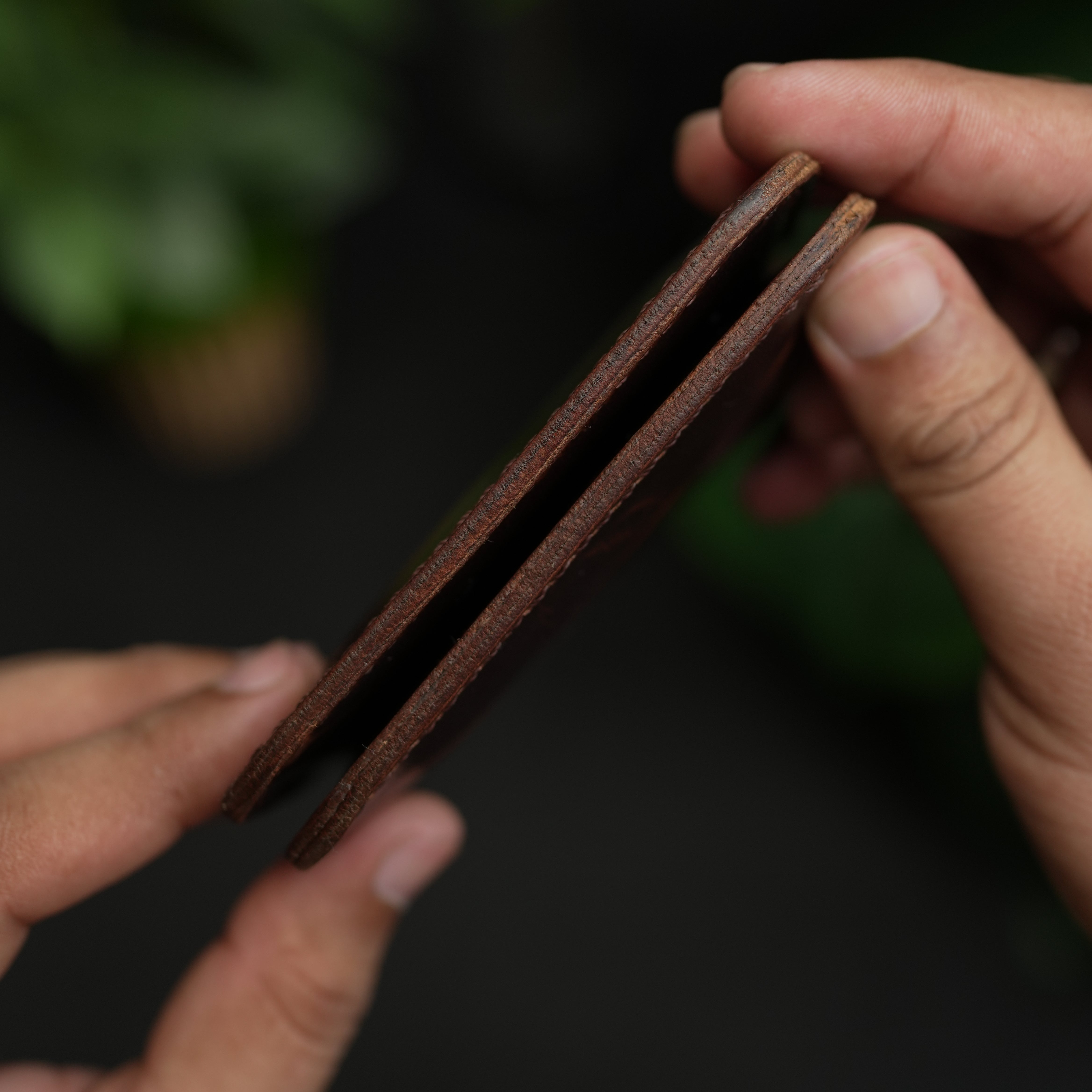 Close-up of hands holding a brown leather wallet against a dark background
