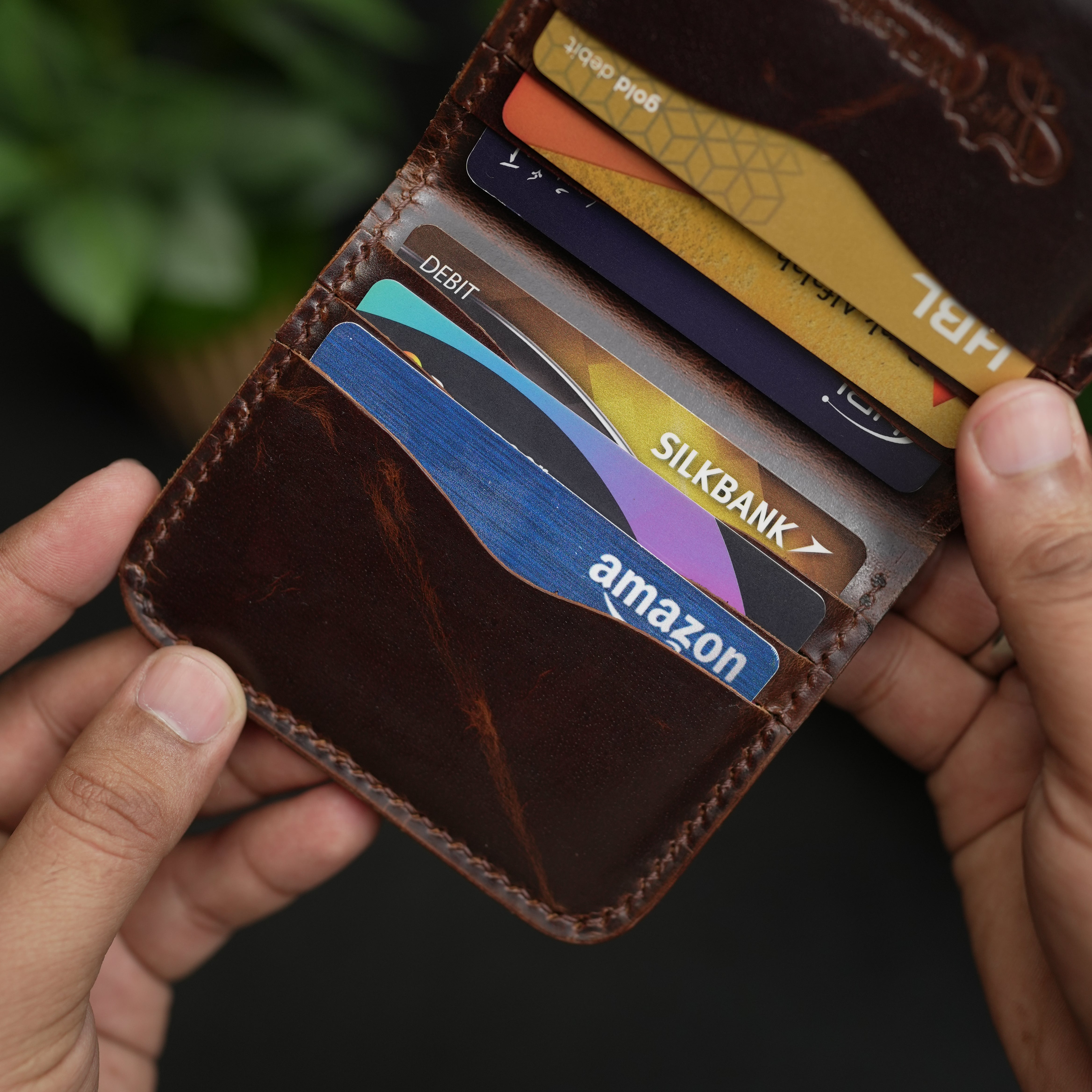 Hand holding a brown leather wallet with various cards including Amazon and SilkBank.