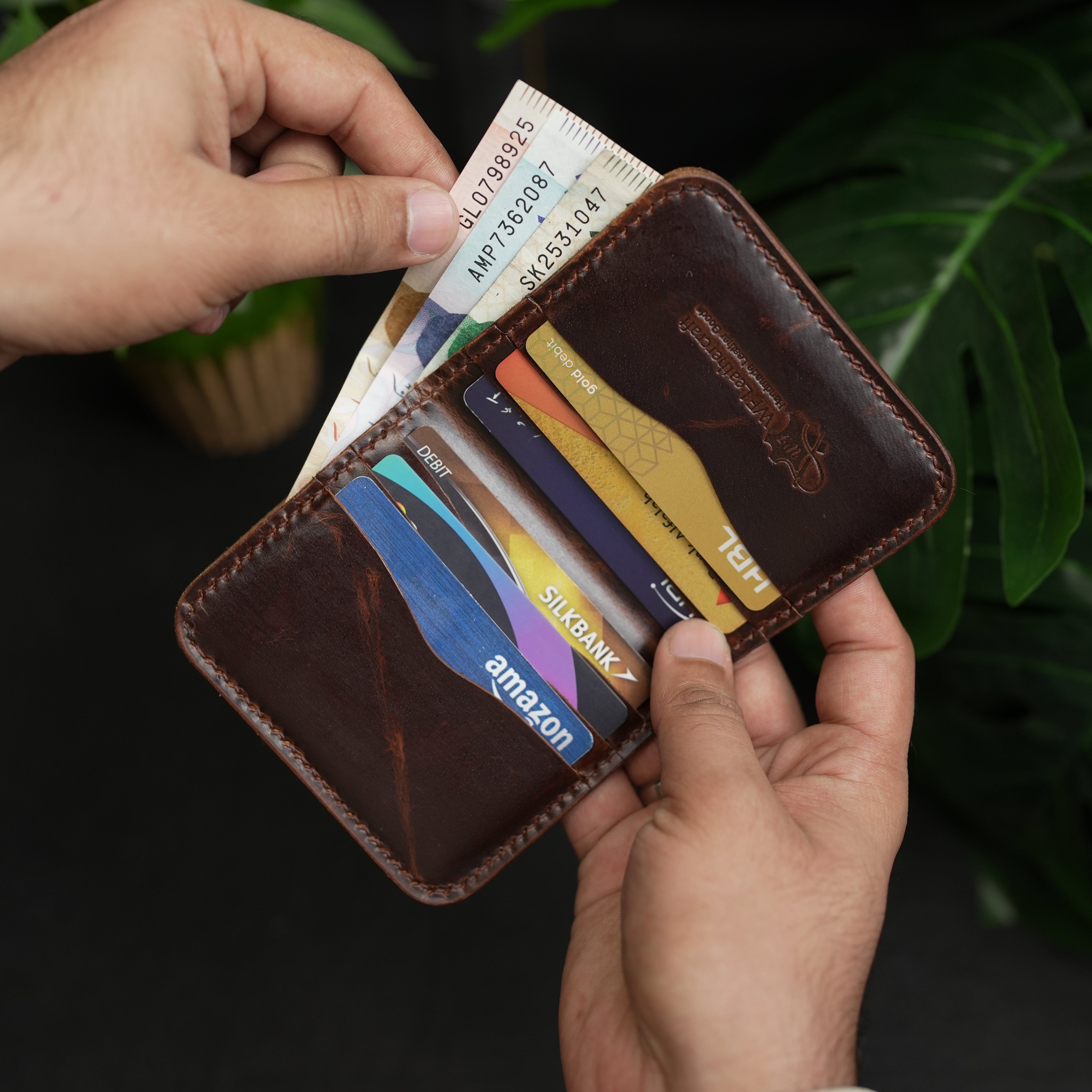 Brown leather wallet with various credit cards held by a person against a dark background.