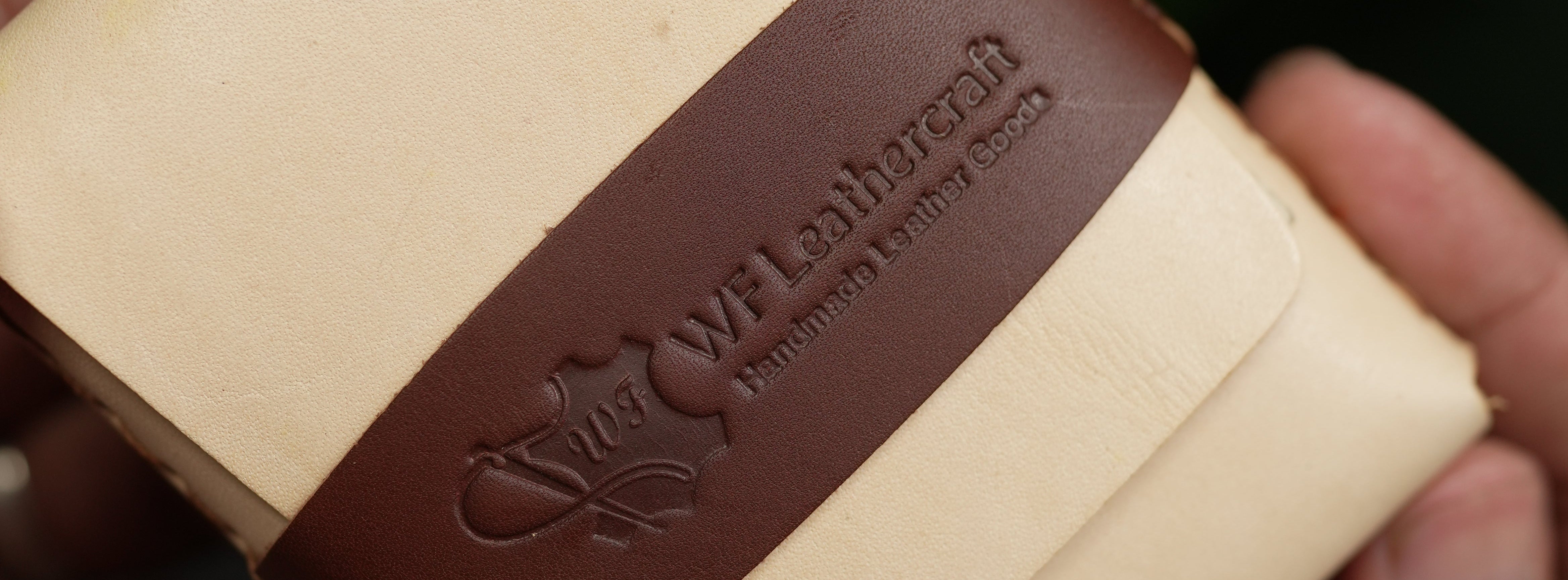 Beige notebook with brown leather strap held by a hand against a blurred green background