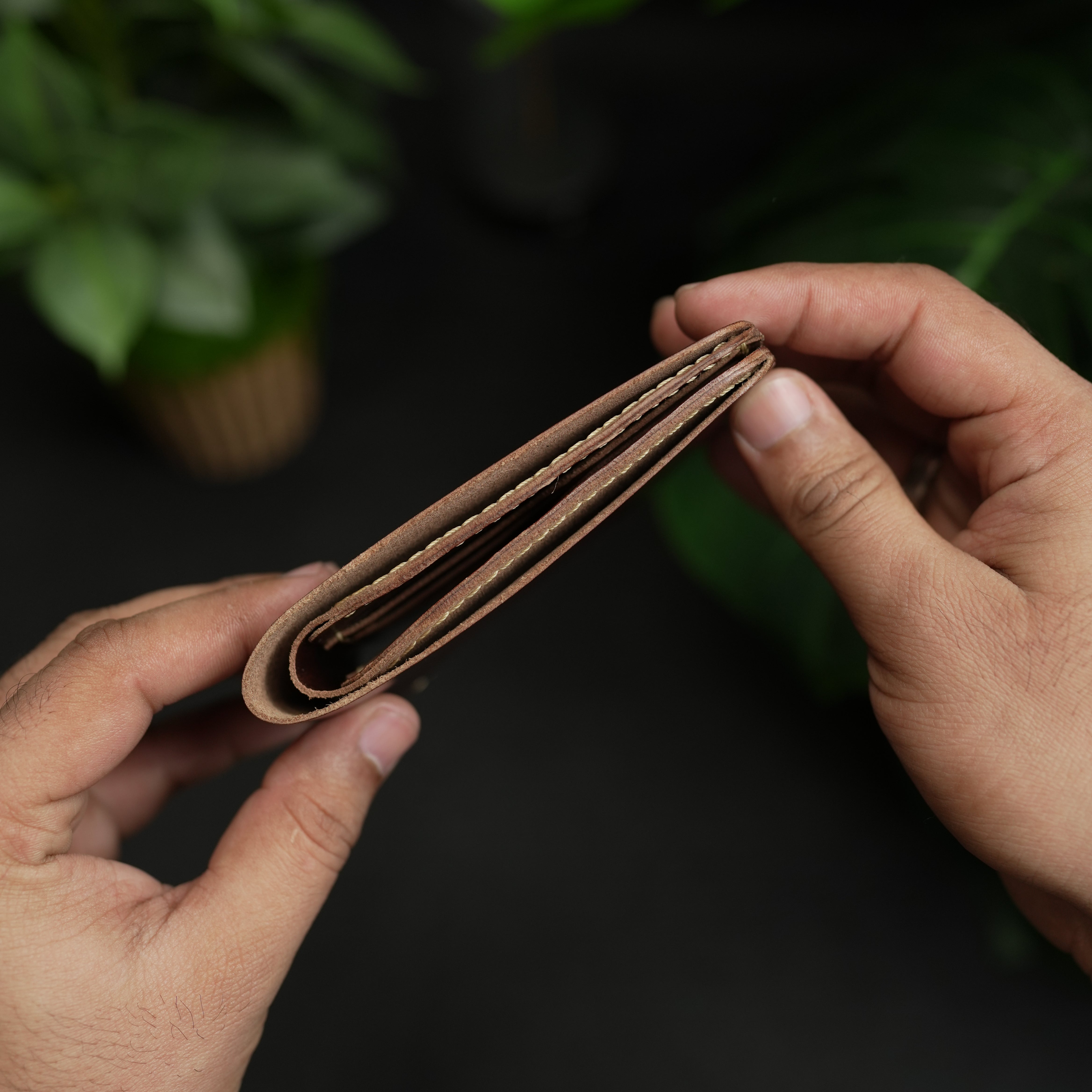 Brown leather wallet held by hands with a dark background