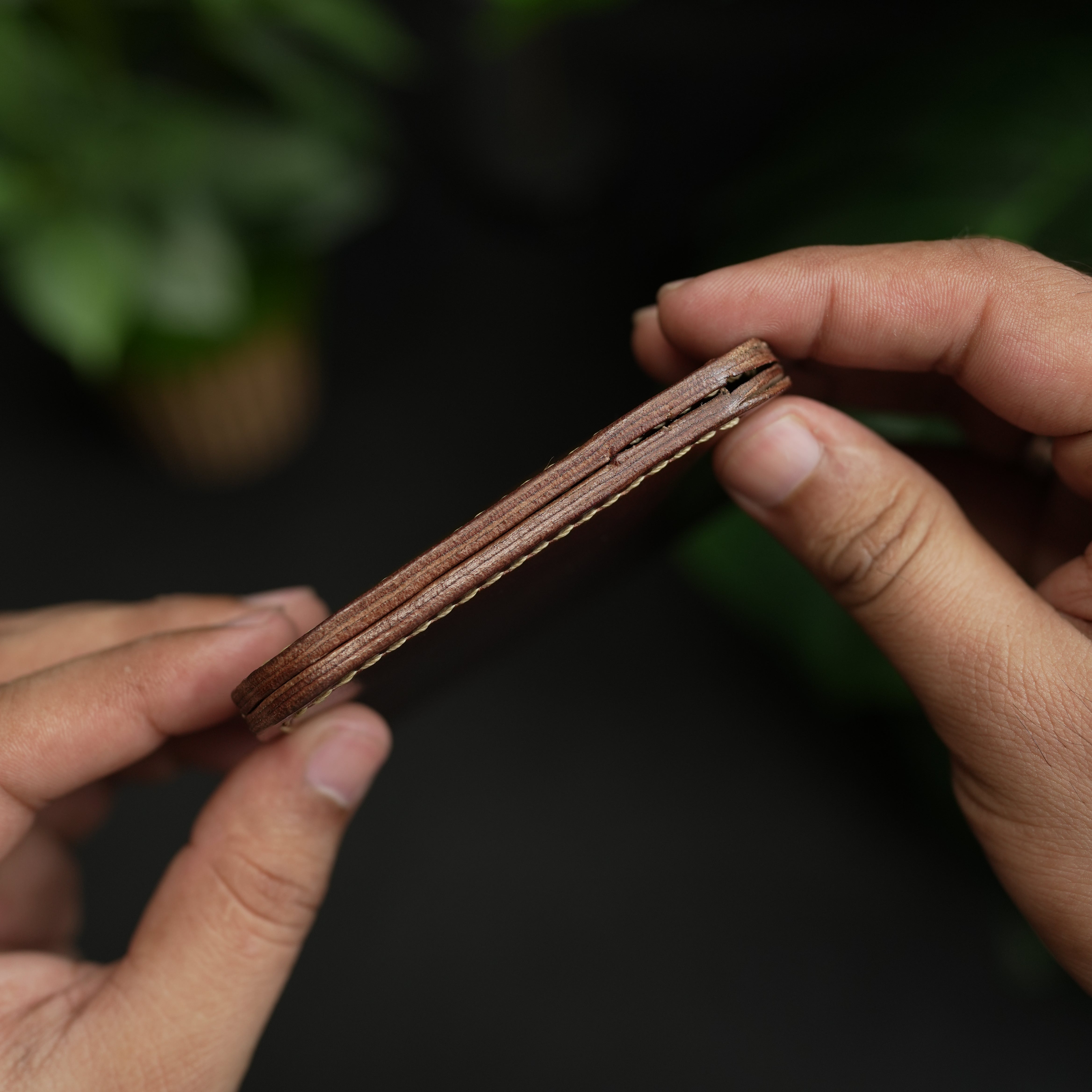 Close-up of hands holding a brown leather wallet against a dark background