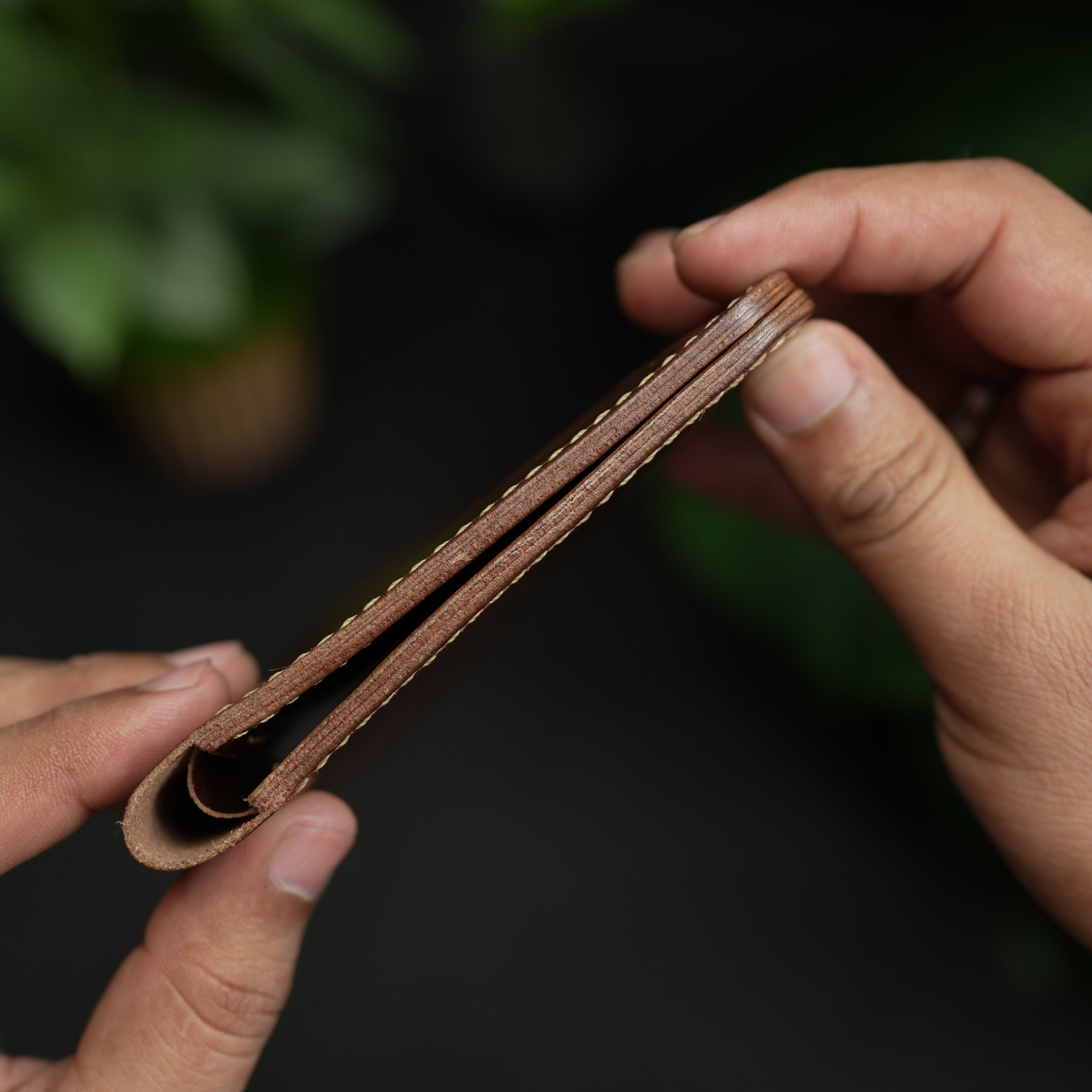 Close-up of hands holding a brown leather strap against a dark background