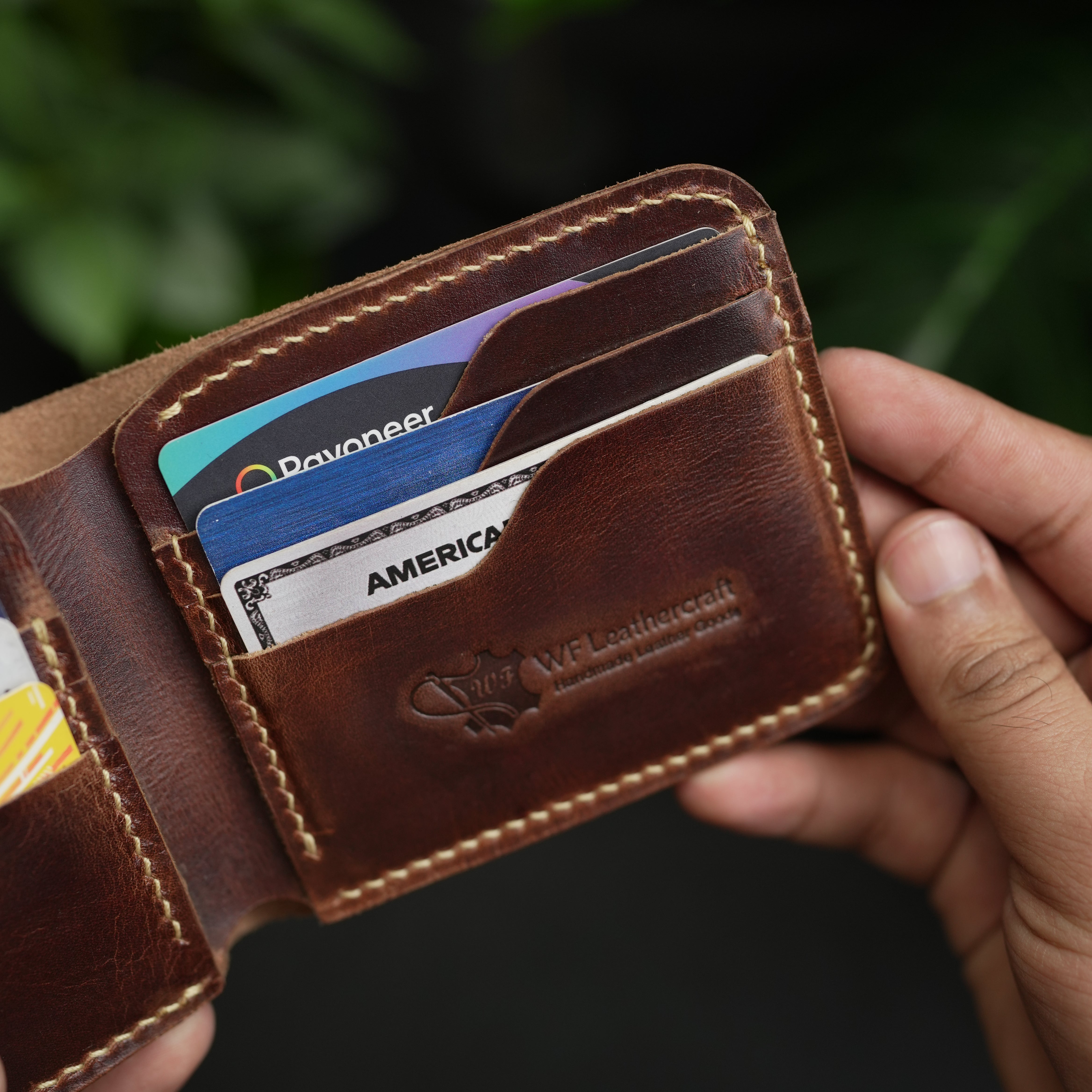 Brown leather wallet with cards held by a hand against a dark background