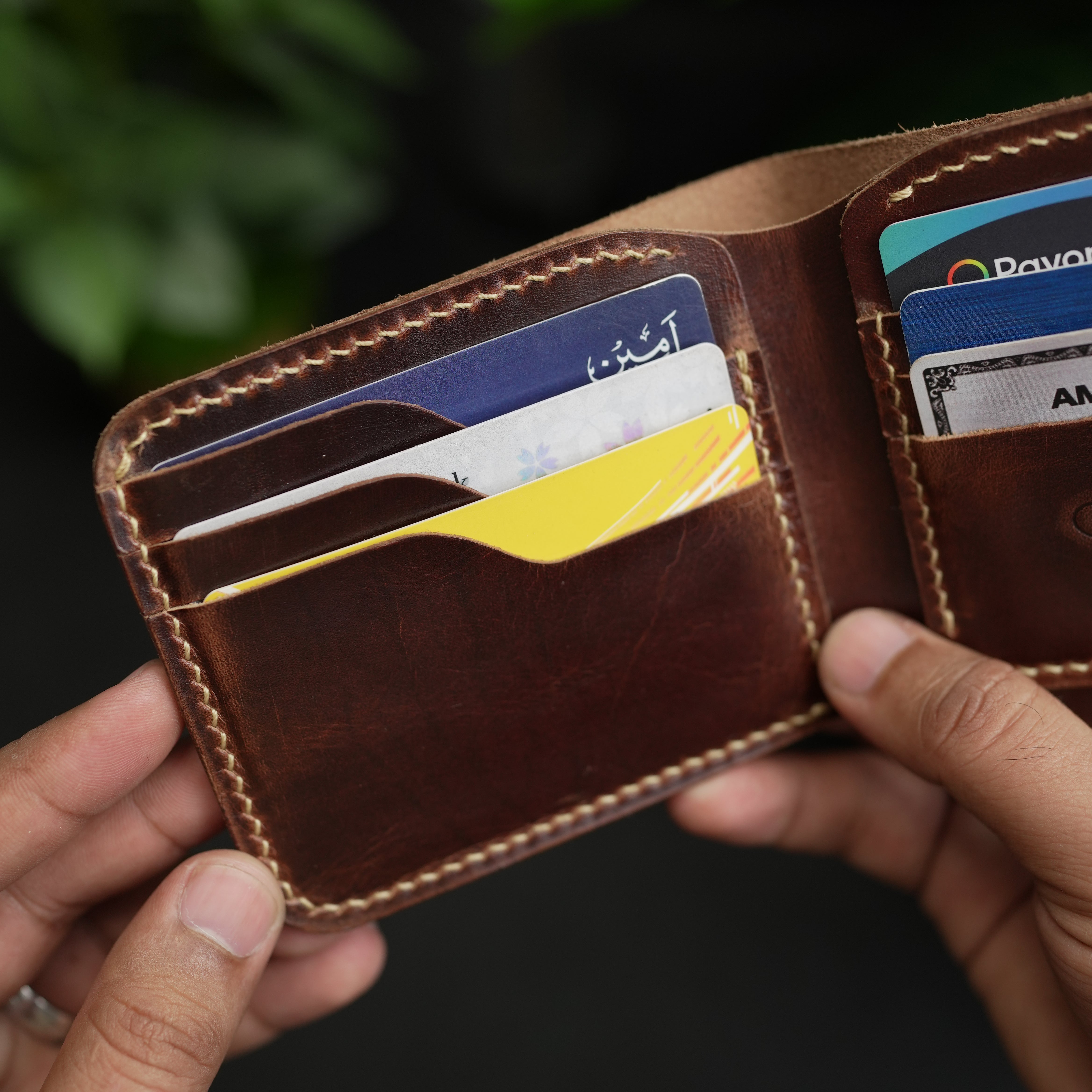 Brown leather wallet with cards held by a hand against a dark background