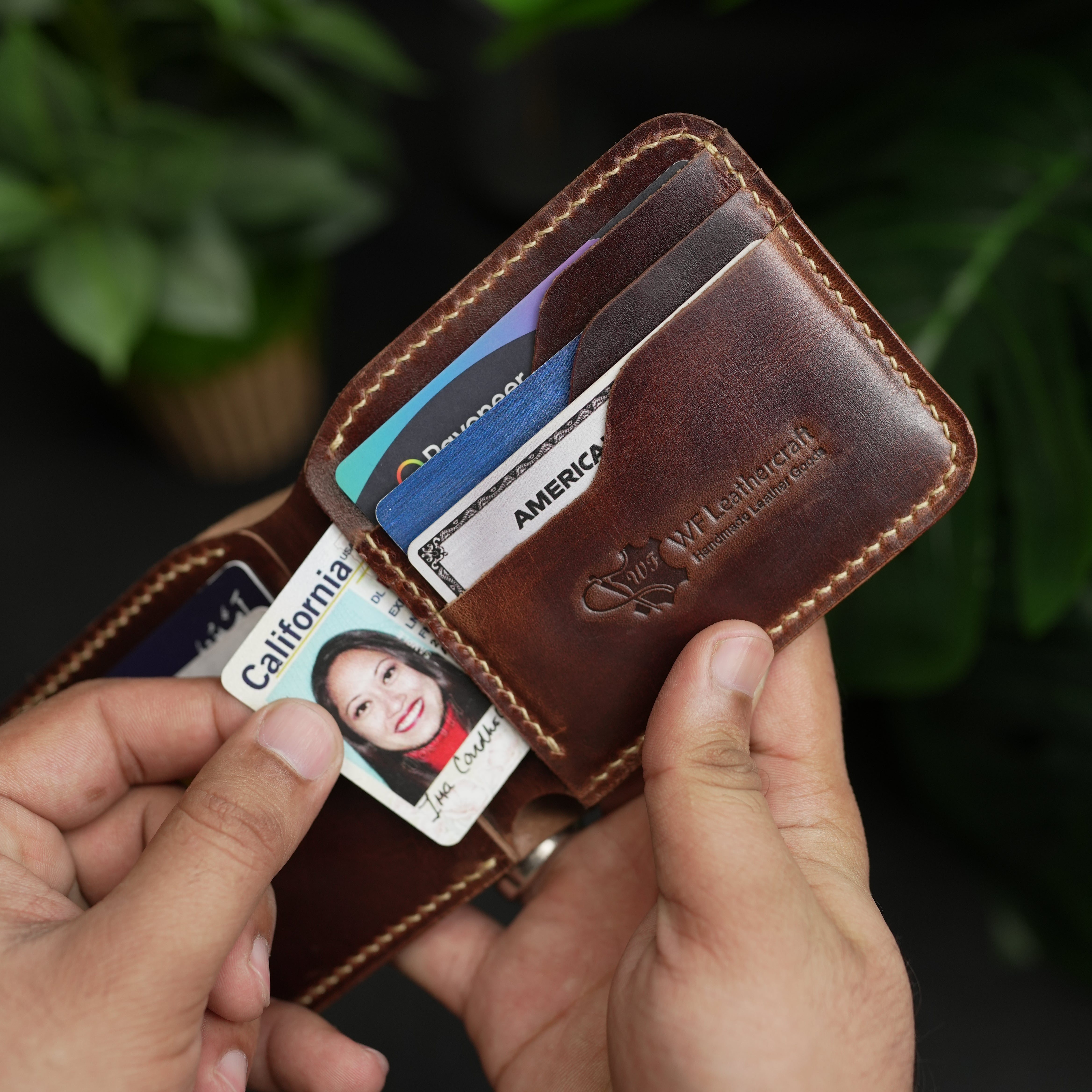 Brown leather wallet with cards and a photo card held by a hand against a blurred green background