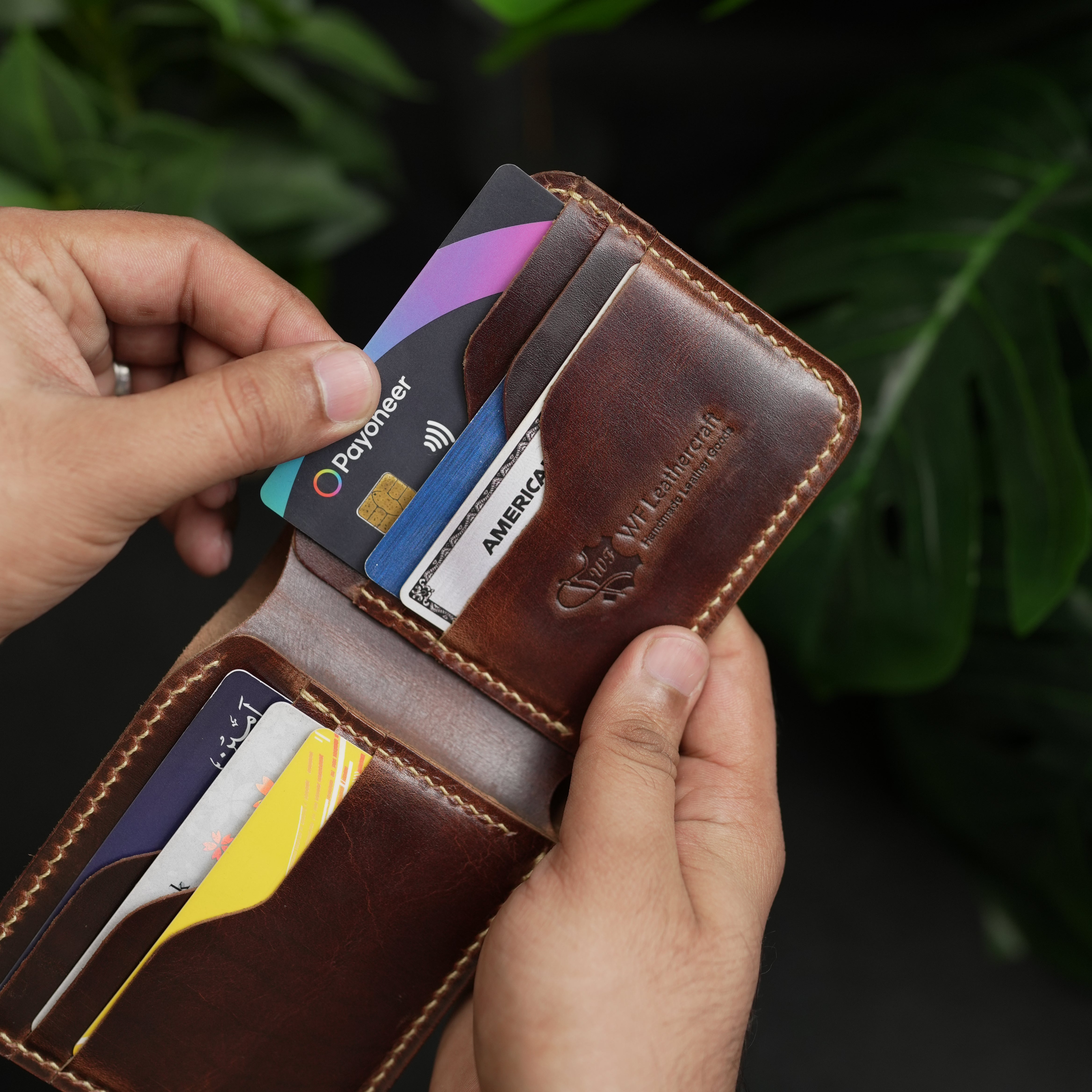 Brown leather wallet with cards held by a hand against a dark background