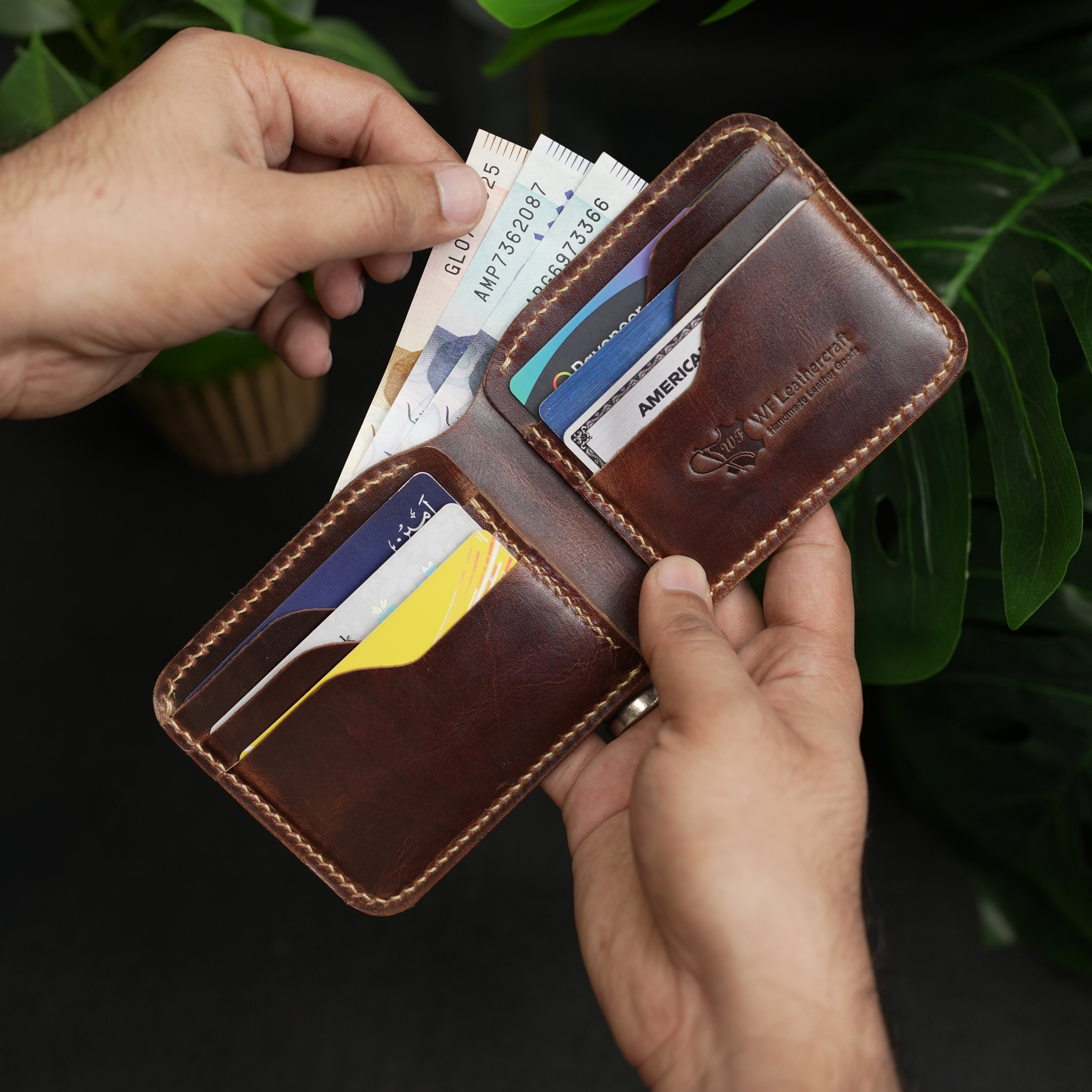 Brown leather wallet with cards held open by hands against a dark background