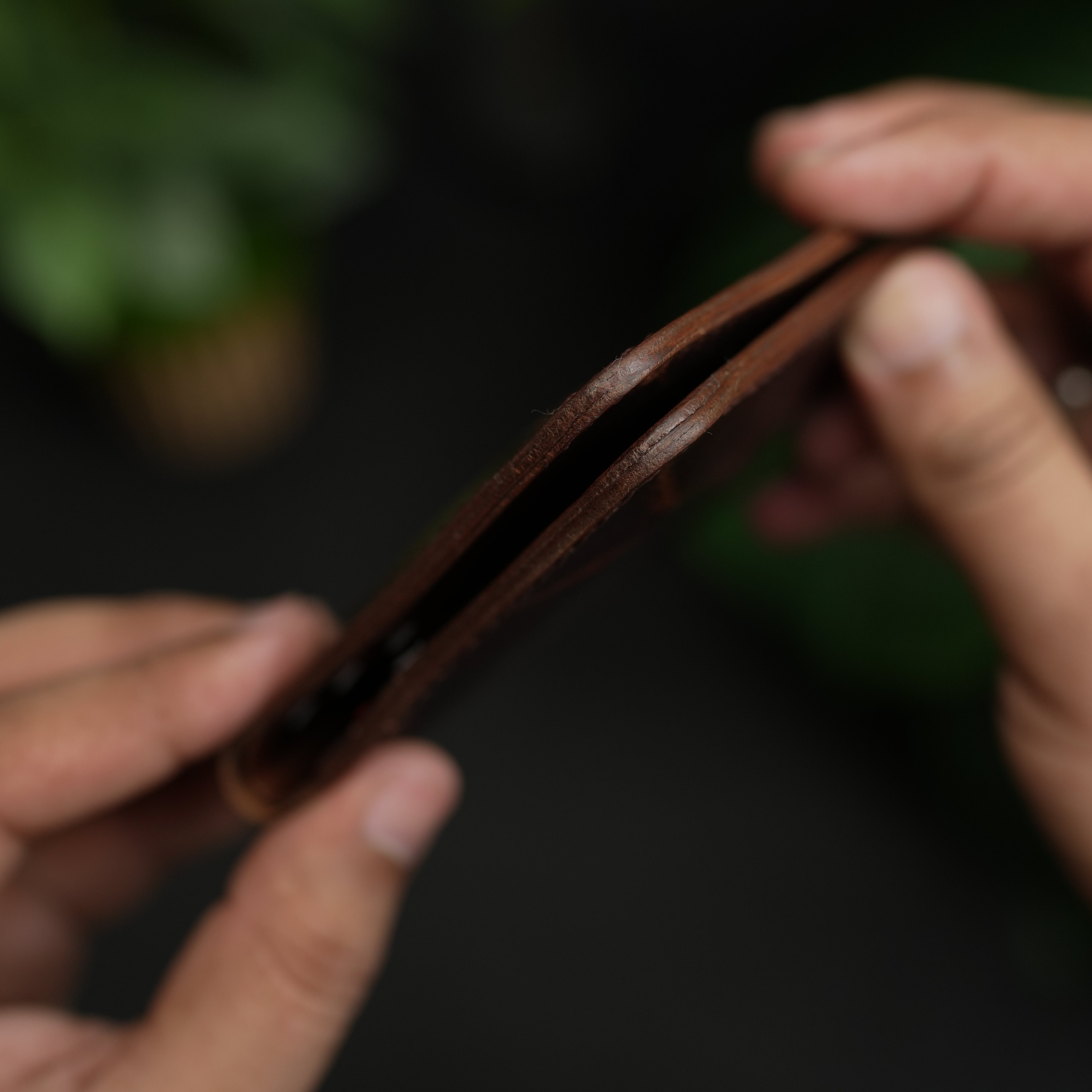 Close-up of hands holding a brown leather belt against a dark background