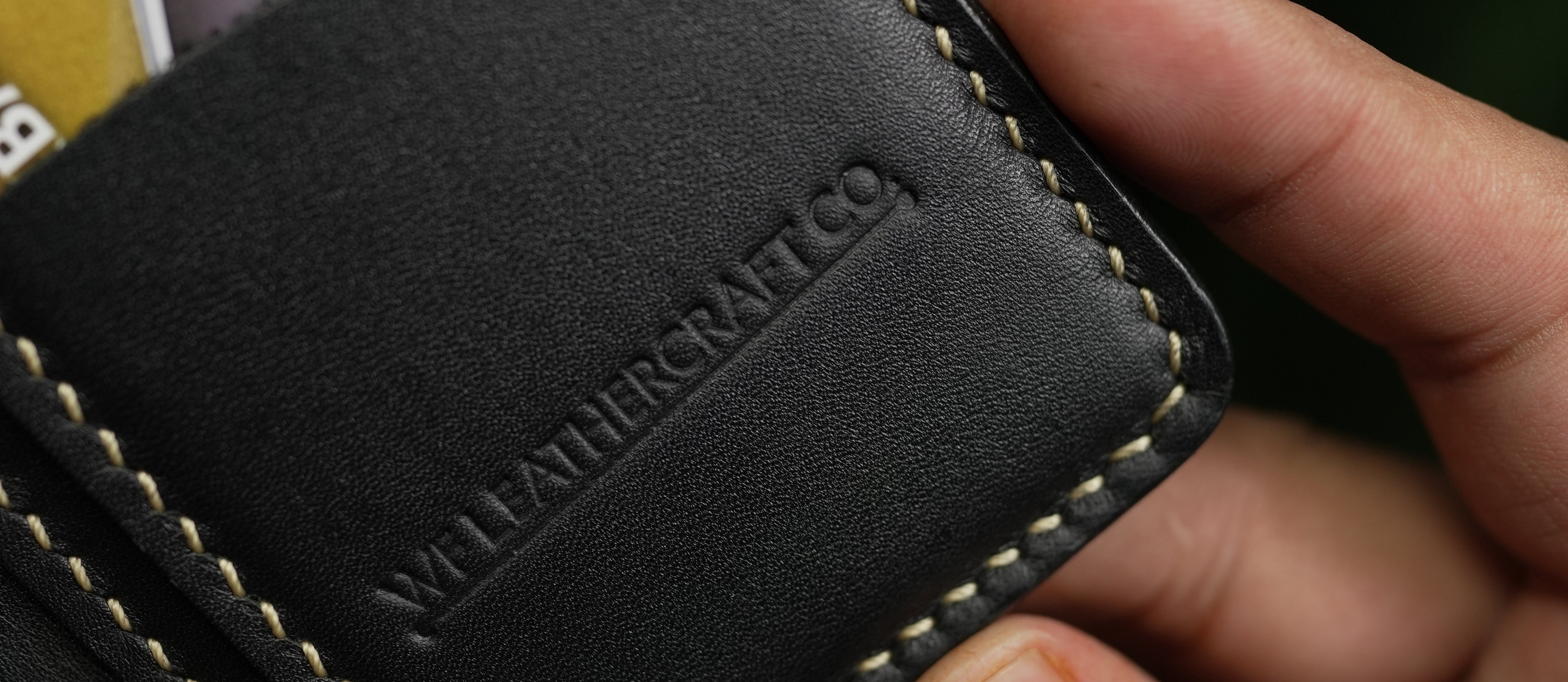 Black leather wallet with brand name held by a hand, with blurred cardholder in the background