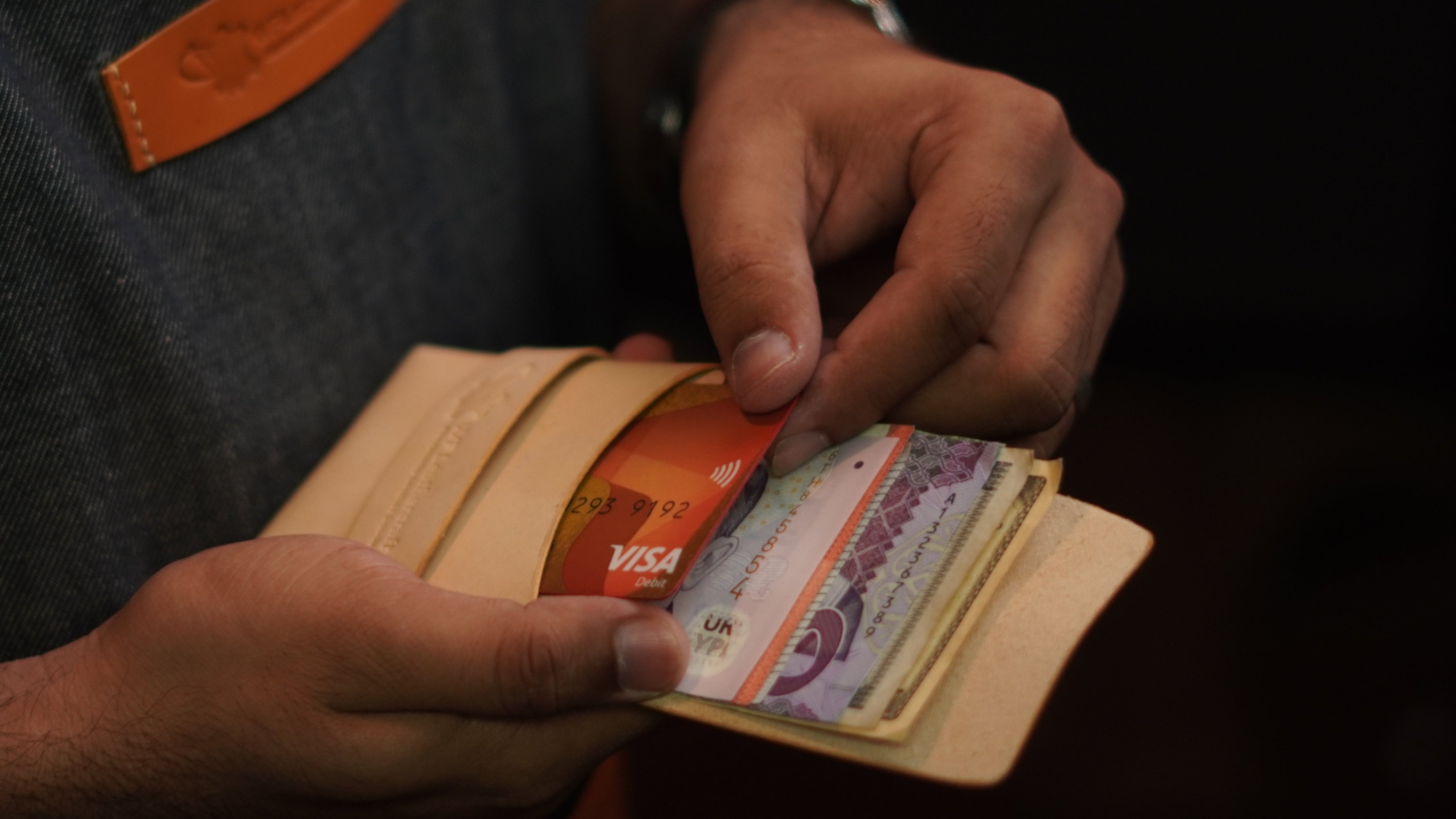 Person holding a wallet with currency notes against a dark background